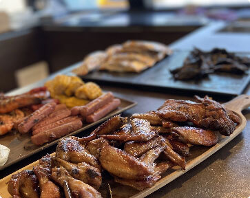 Platter of barbecued chicken wings and drumsticks, with other dishes like grilled shrimp and sausages.