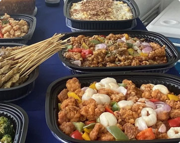 Catered buffet featuring trays of fried chicken, satay skewers, and fried rice.
