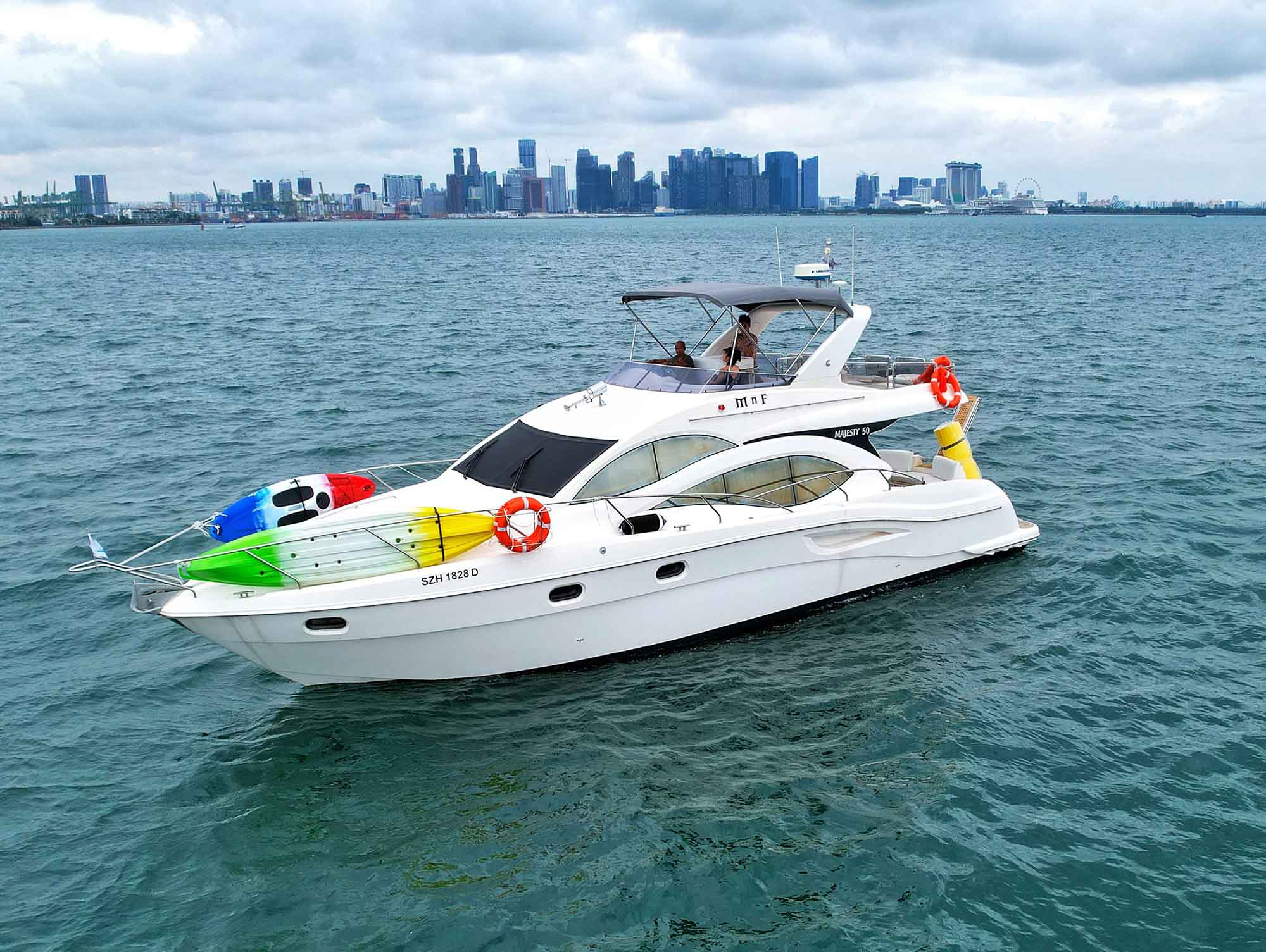 Modern white motor yacht, a Majesty 50, floats on the water with two colorful kayaks strapped to its bow.