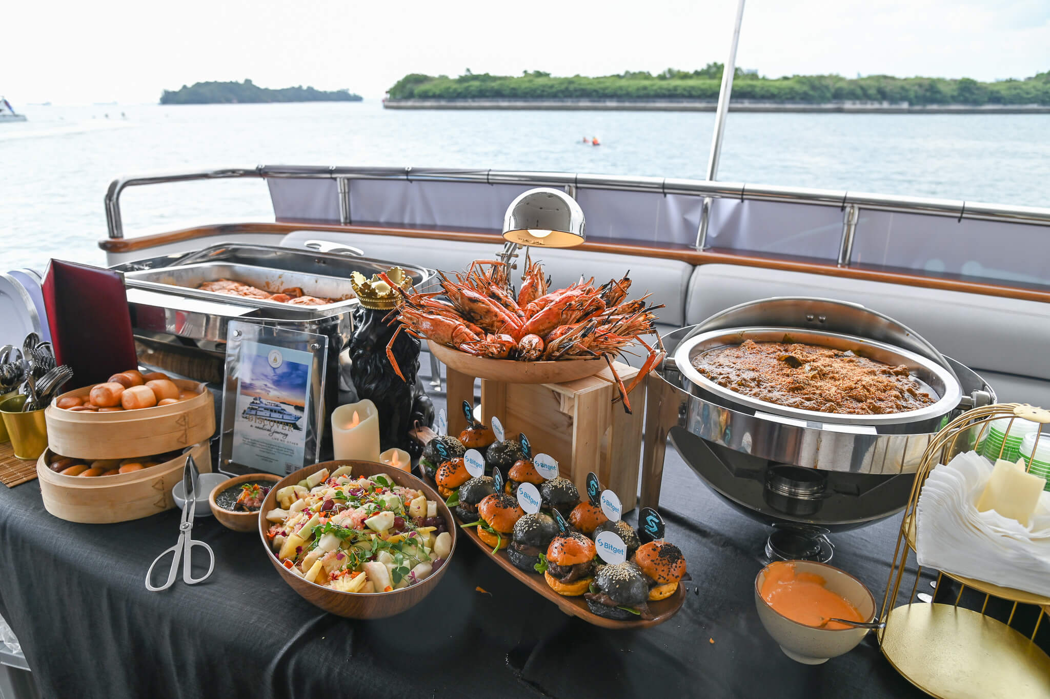 A full catering spread on a yacht with king prawns, salads, and mini burgers.