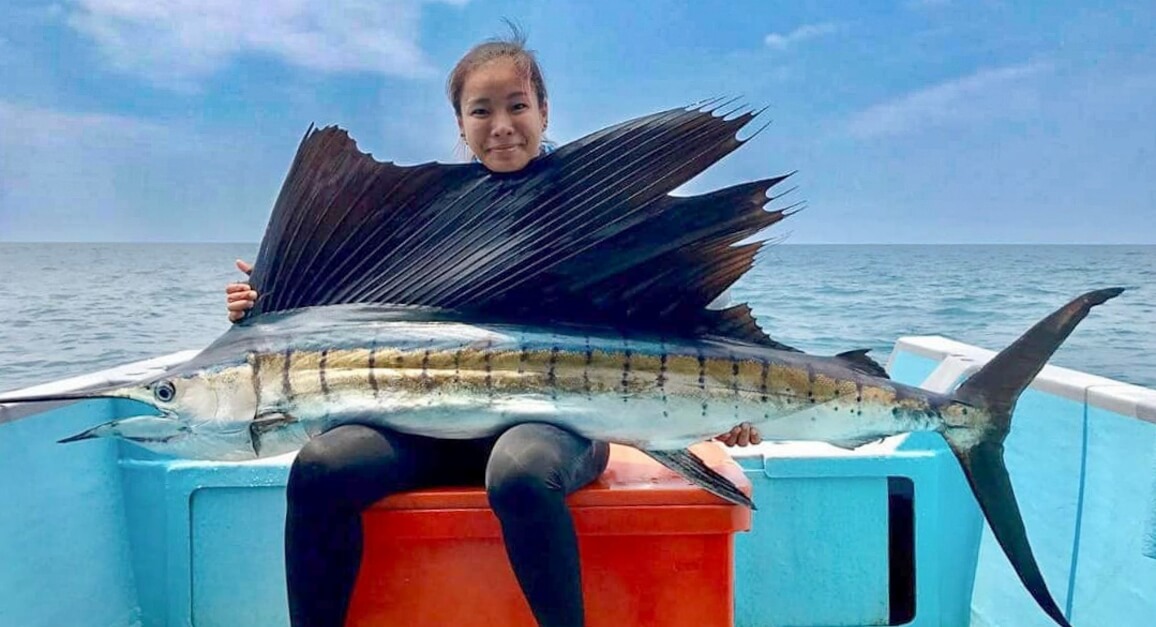 A woman on a boat holds a large sailfish across her lap.