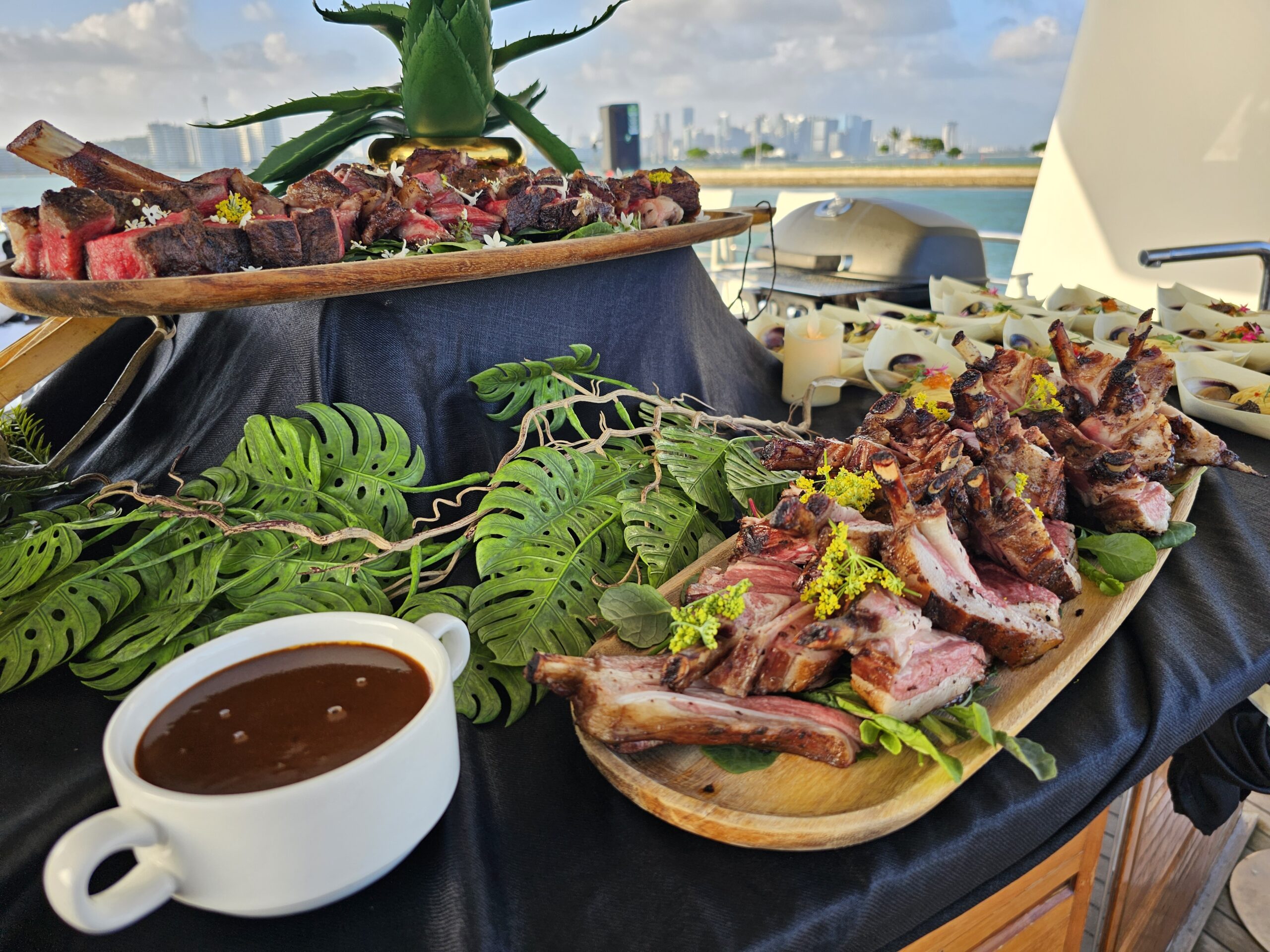 Gourmet buffet on a yacht with sliced meat, lamb, and a city skyline.
