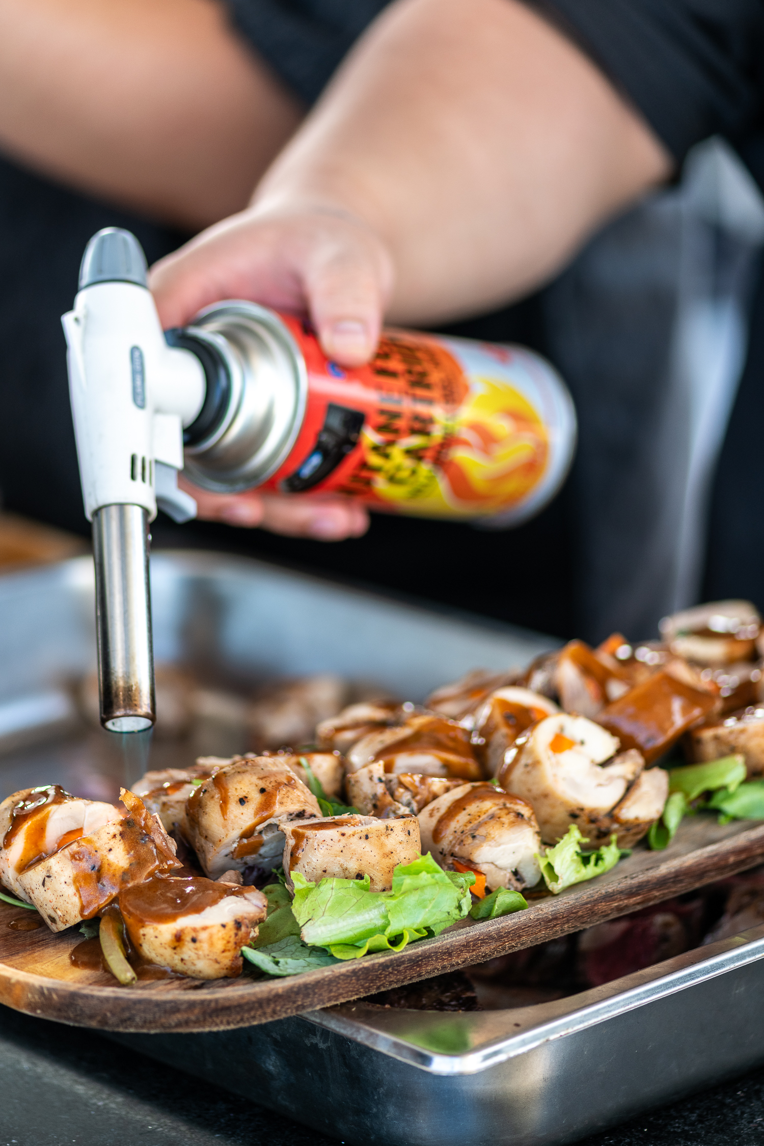 Chef uses a culinary blowtorch to sear sliced meat on a wooden platter.